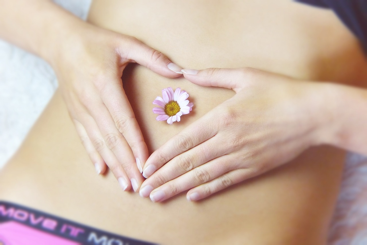 Woman forming a heart with her hands and a flower is shown on top of her belly button